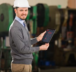 Worker in a factory holding a tablet looking at the camera with a white safety hat on