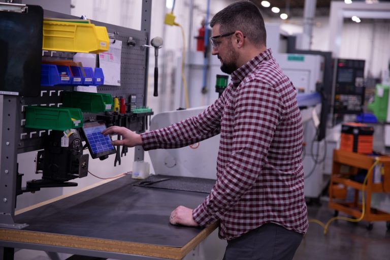 Factory Worker in a plaid shirt using a FactoryWiz Tablet attached to a Machine.